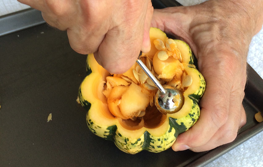 close up image of hands scooping out the inside of an acorn squash