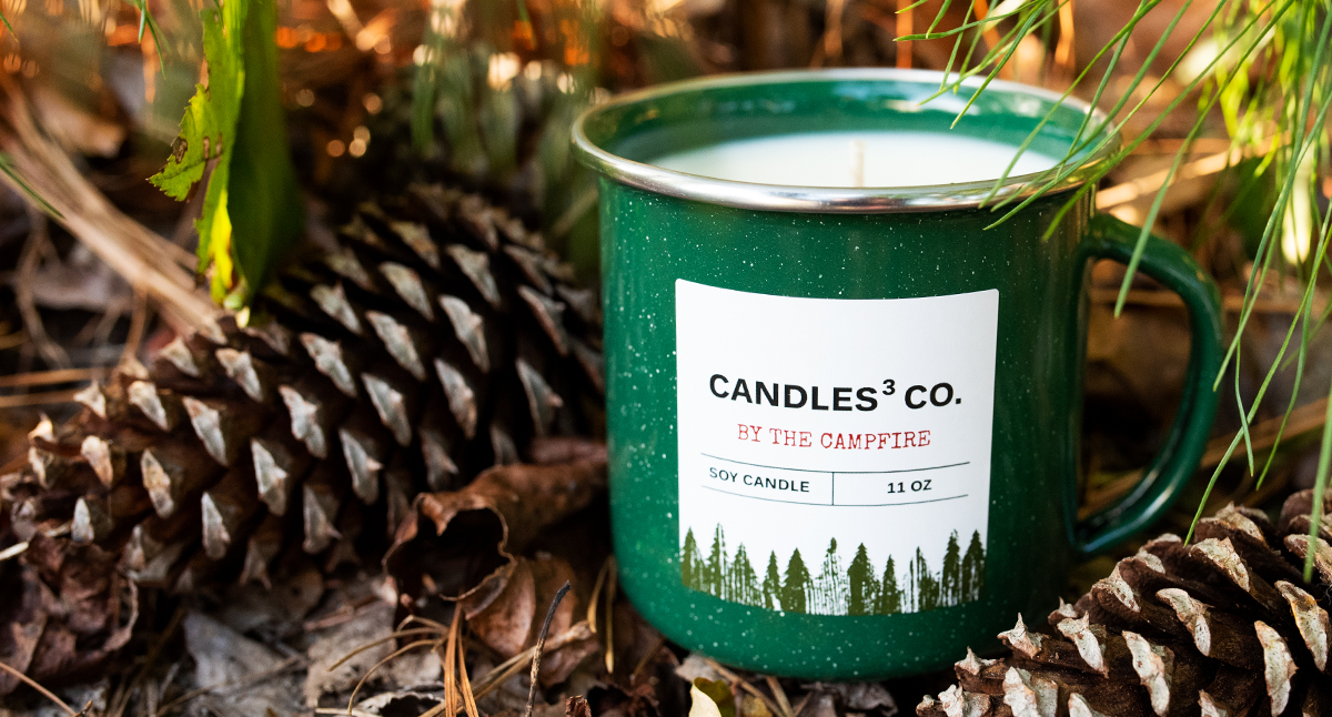 A green enamel mug candle next to pinecones and pine branches.