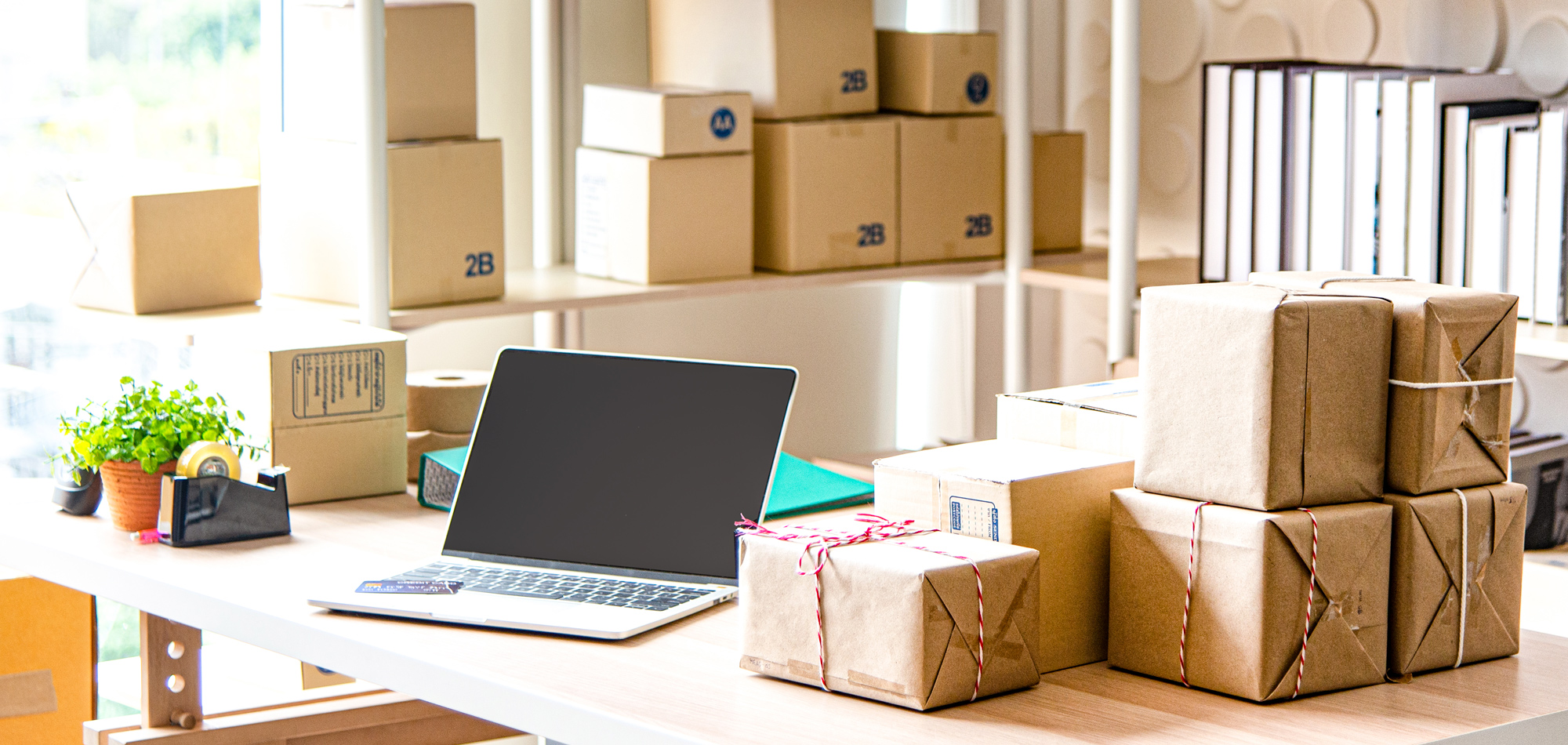 An open laptop next to a pile of boxes ready to ship.