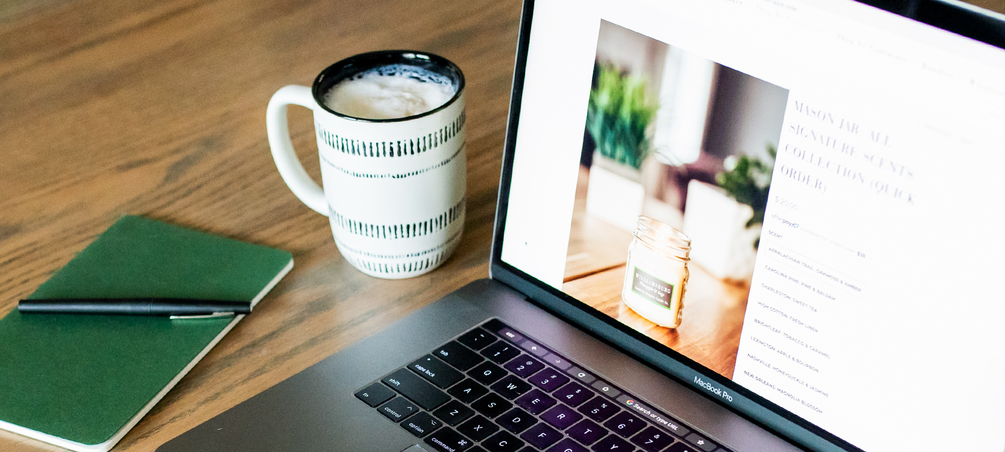 Open laptop next to a latte and notebook with pen.