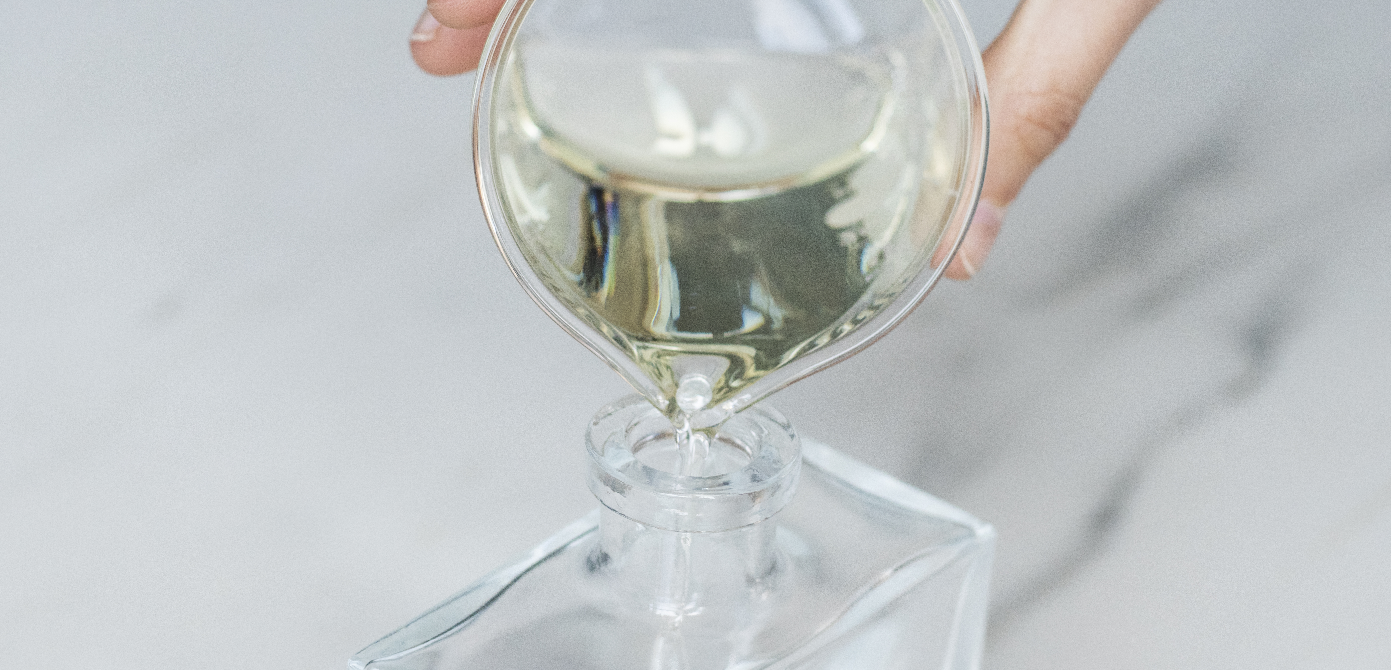 Close up of fragrance oil and reed diffuser base being poured into a glass jar.