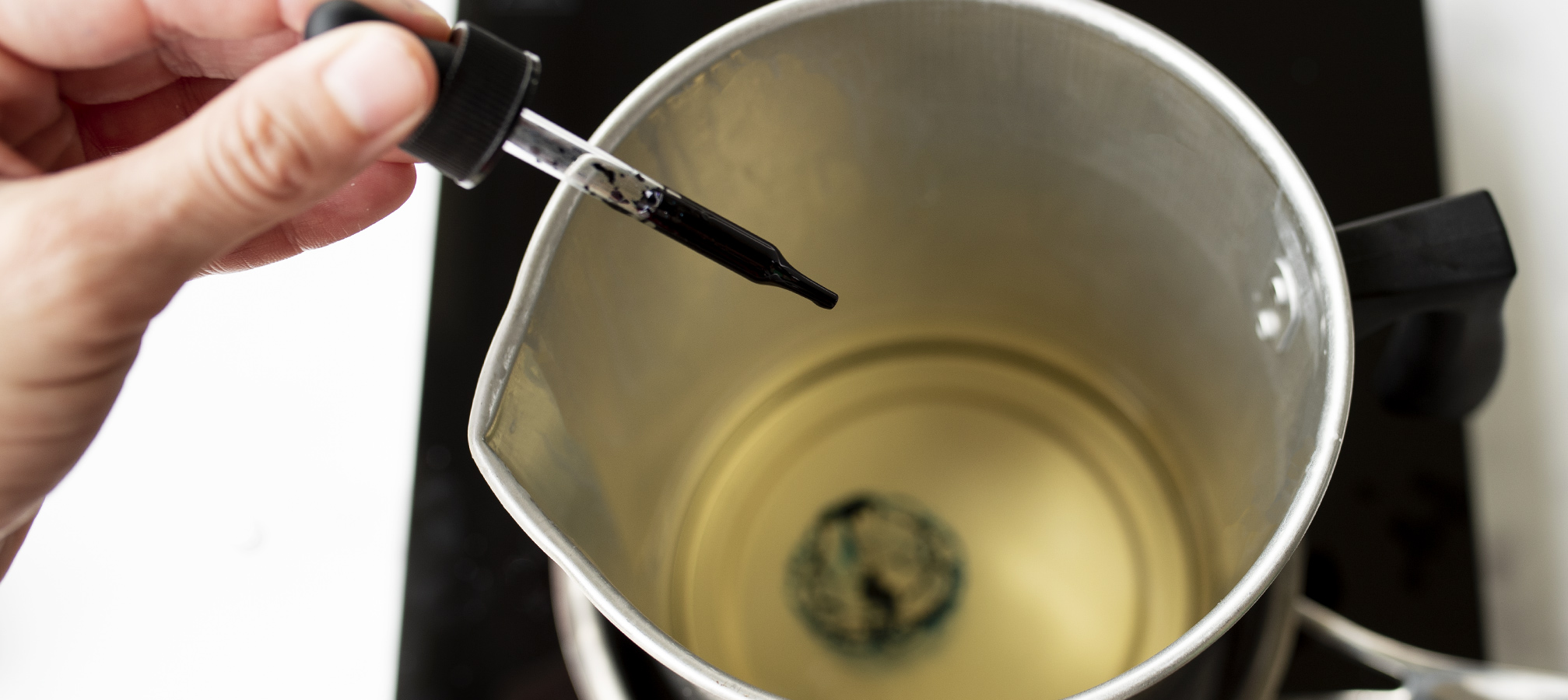 Adding blue candle dye with a dropper into a pouring pitcher with melted soy wax.