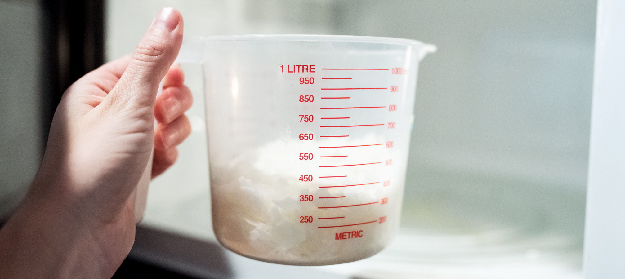 Placing soy wax flakes in a plastic pouring pitcher into a microwave.