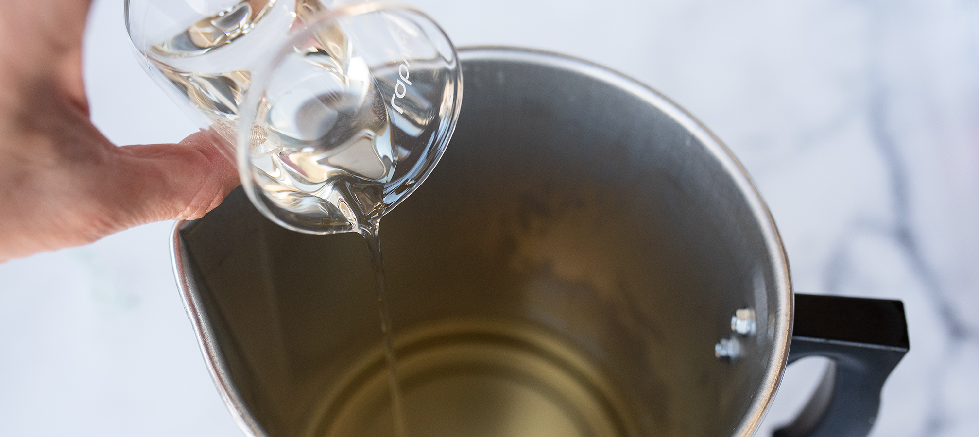 Pouring Cactus Flower and Jade fragrance oil into melted soy wax flakes.