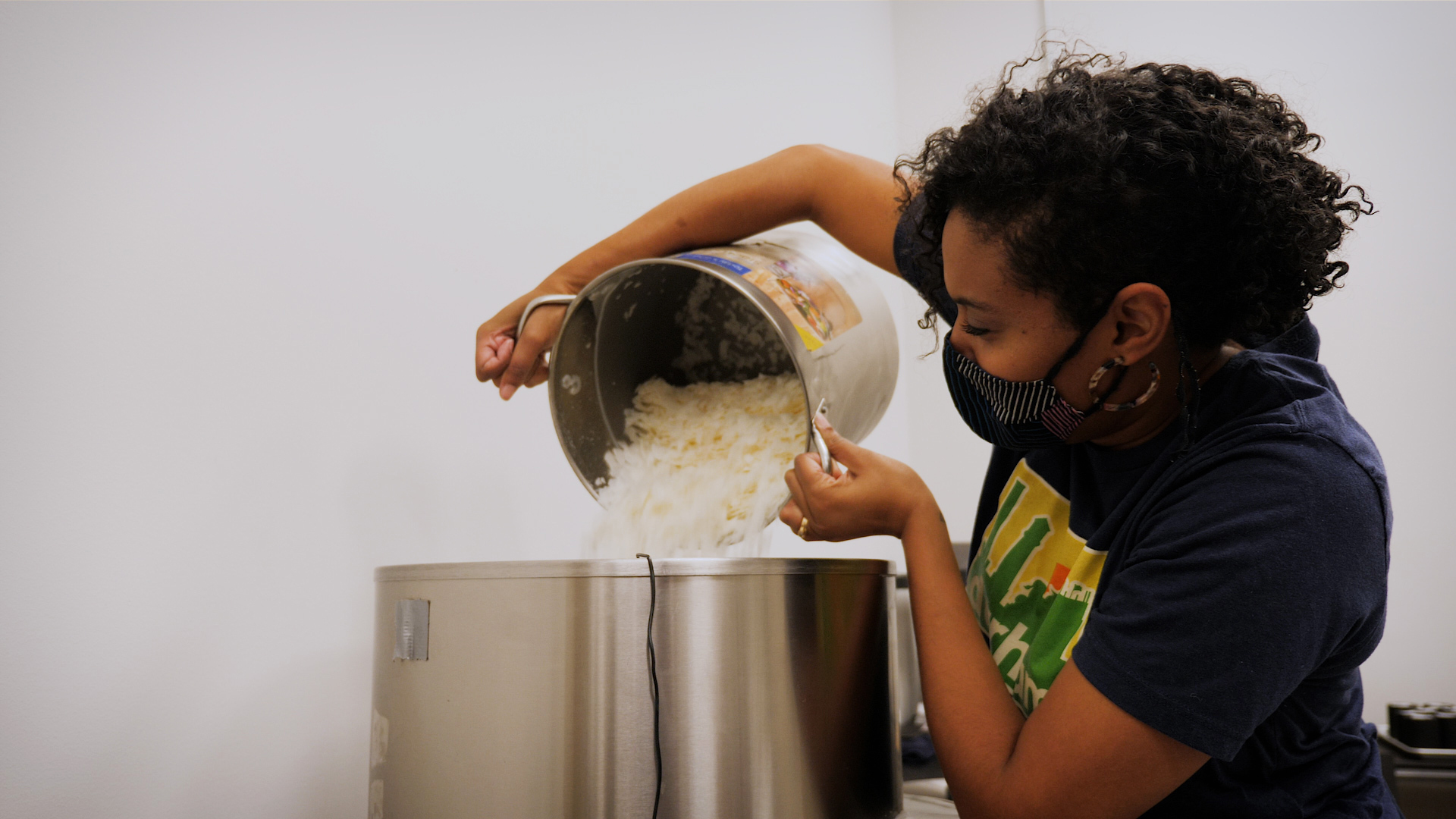 Tiffany from Bright Black pouring wax flakes into a large melting pot. 