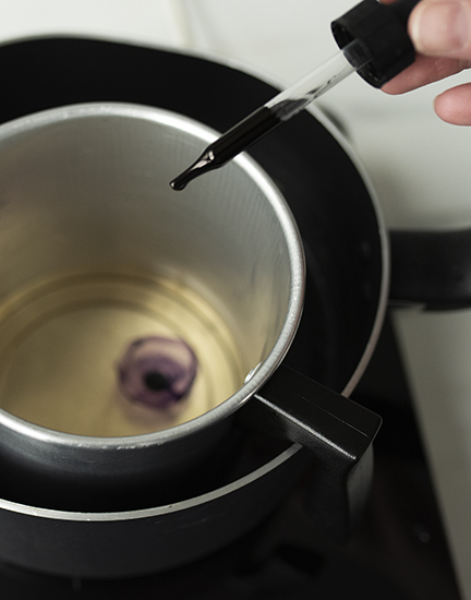 Adding drops of liquid candle dye into melted wax.