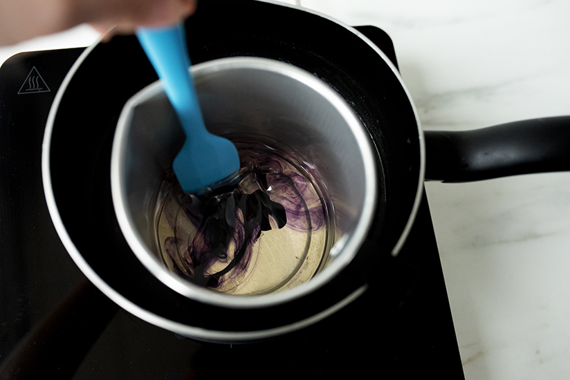 Stirring purple liquid candle dye into wax.