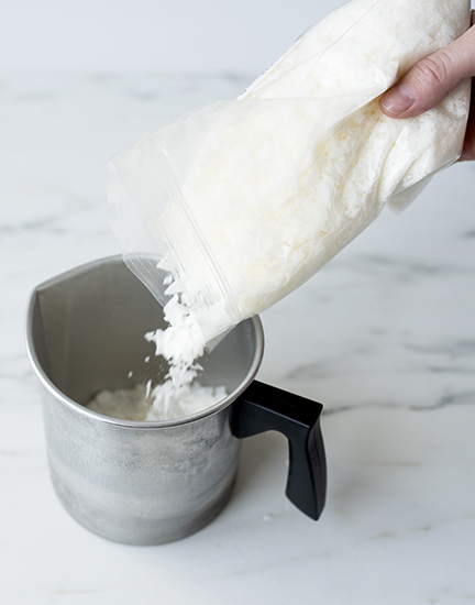 Pouring soy wax flakes into a pouring pitcher.