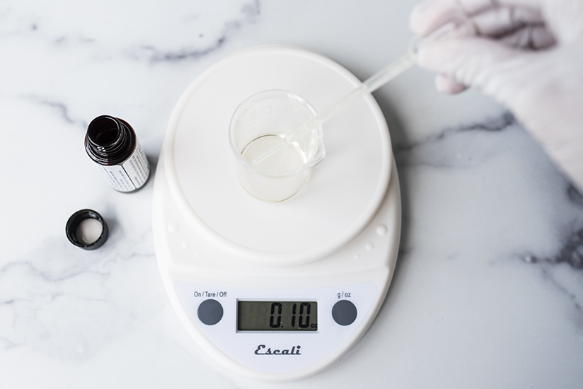 Pipetting fragrance oil into a beaker on a scale.