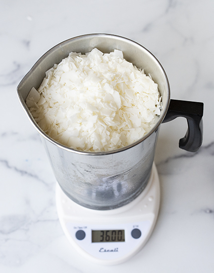 Pouring soy wax flakes into a metal pouring pitcher.