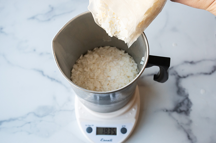 Pouring soy wax flakes into a pouring pitcher.