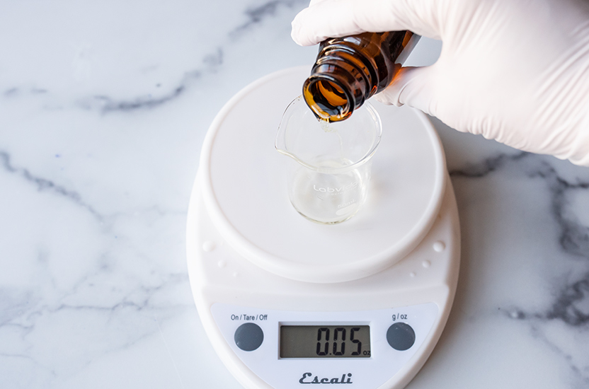 Pouring Lavender essential oil into a glass beaker on a scale.