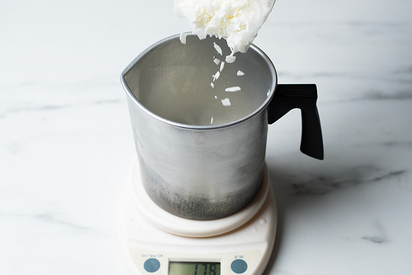 Pouring soy wax flakes into a small pouring pitcher.