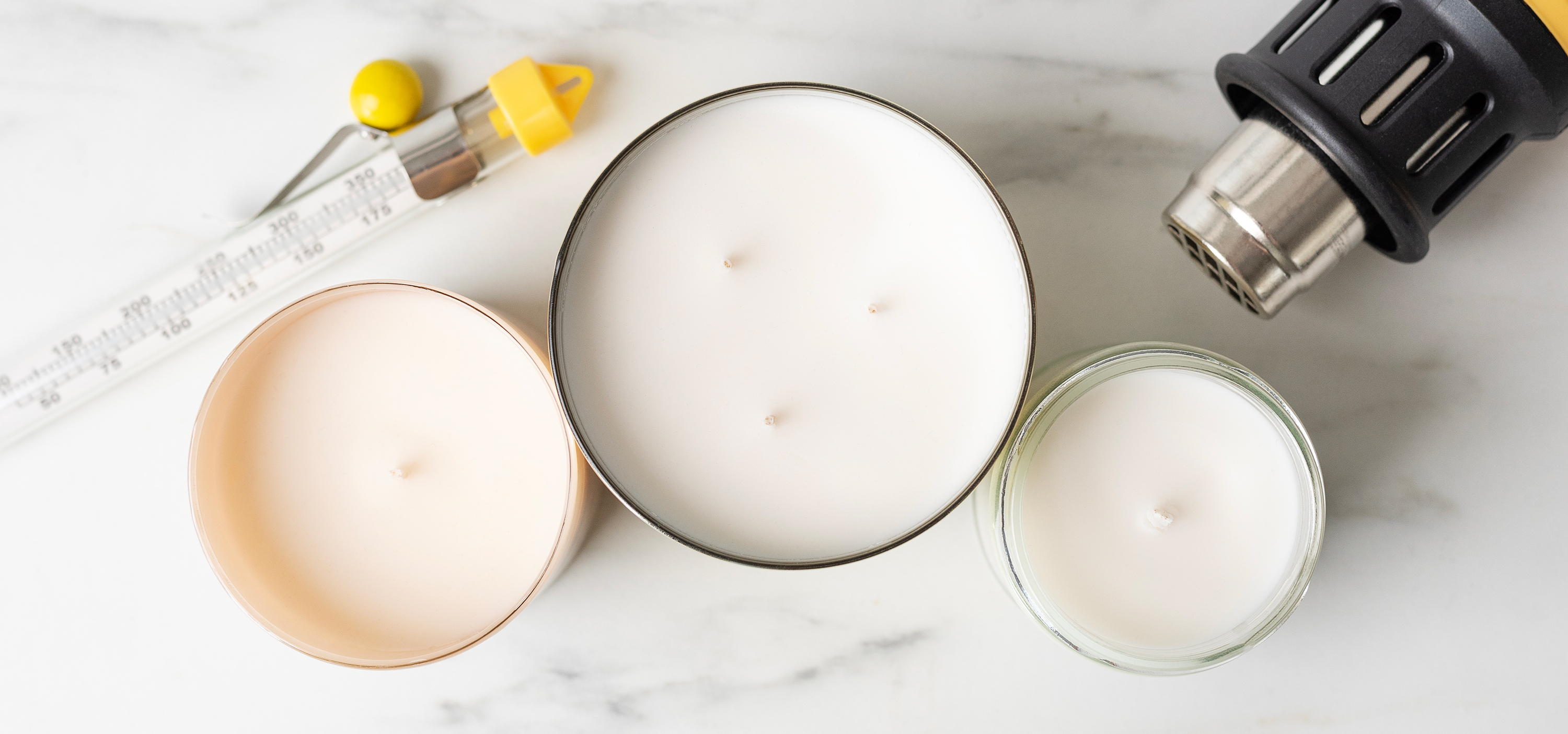 Three unlit candles with smooth tops are flanked by a glass thermometer and heat gun.