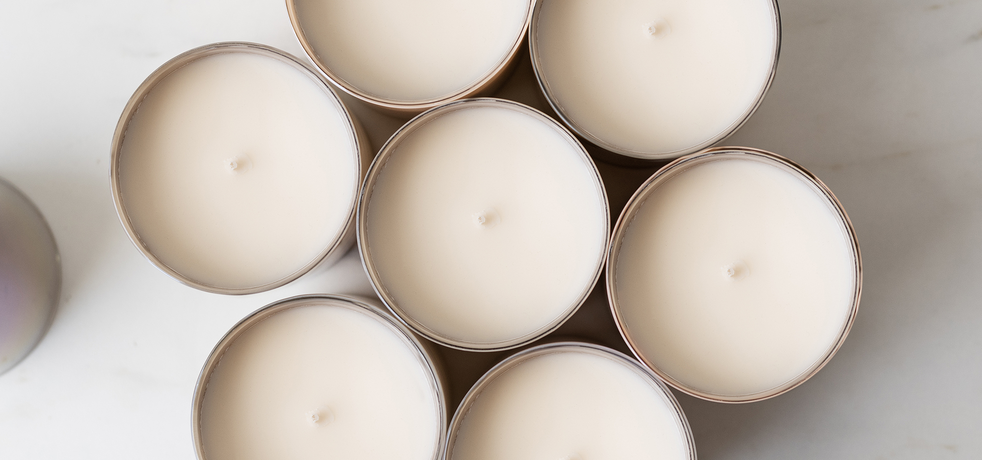 Overhead view of eight candles in taupe iridescent jars on a marble background