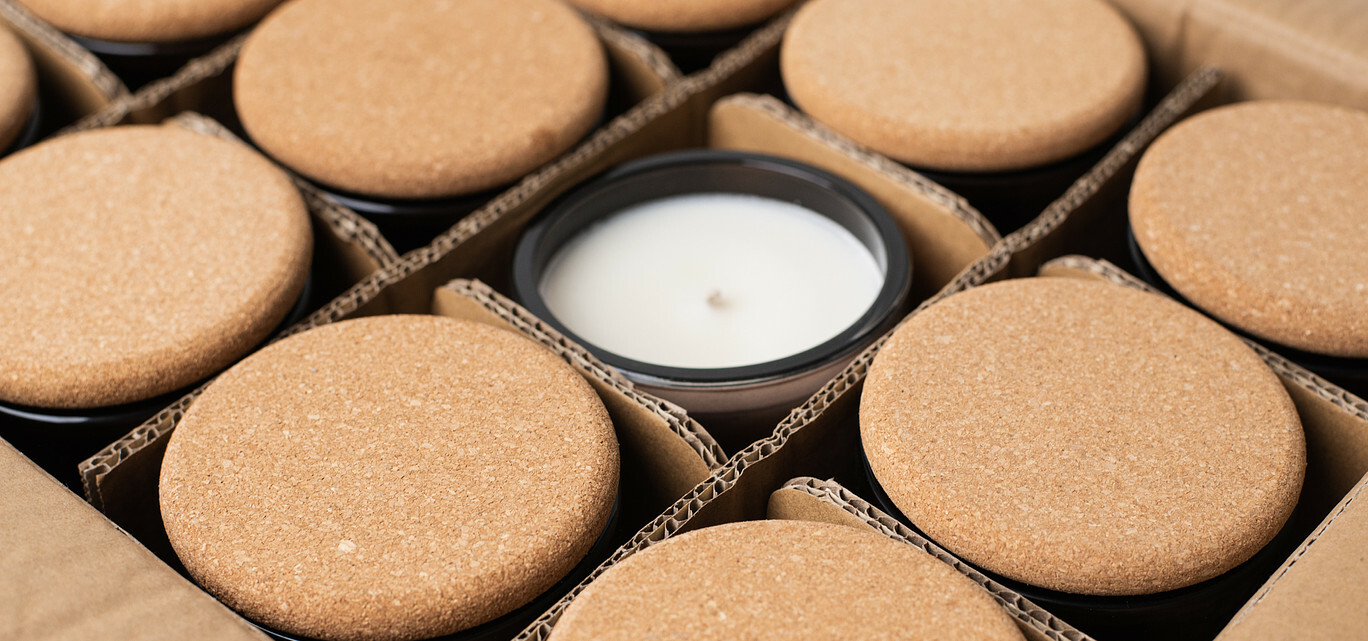 A cardboard box with dividers is filled with black candle jars topped with cord lids. One unlidded candle sits in the middle of the box.