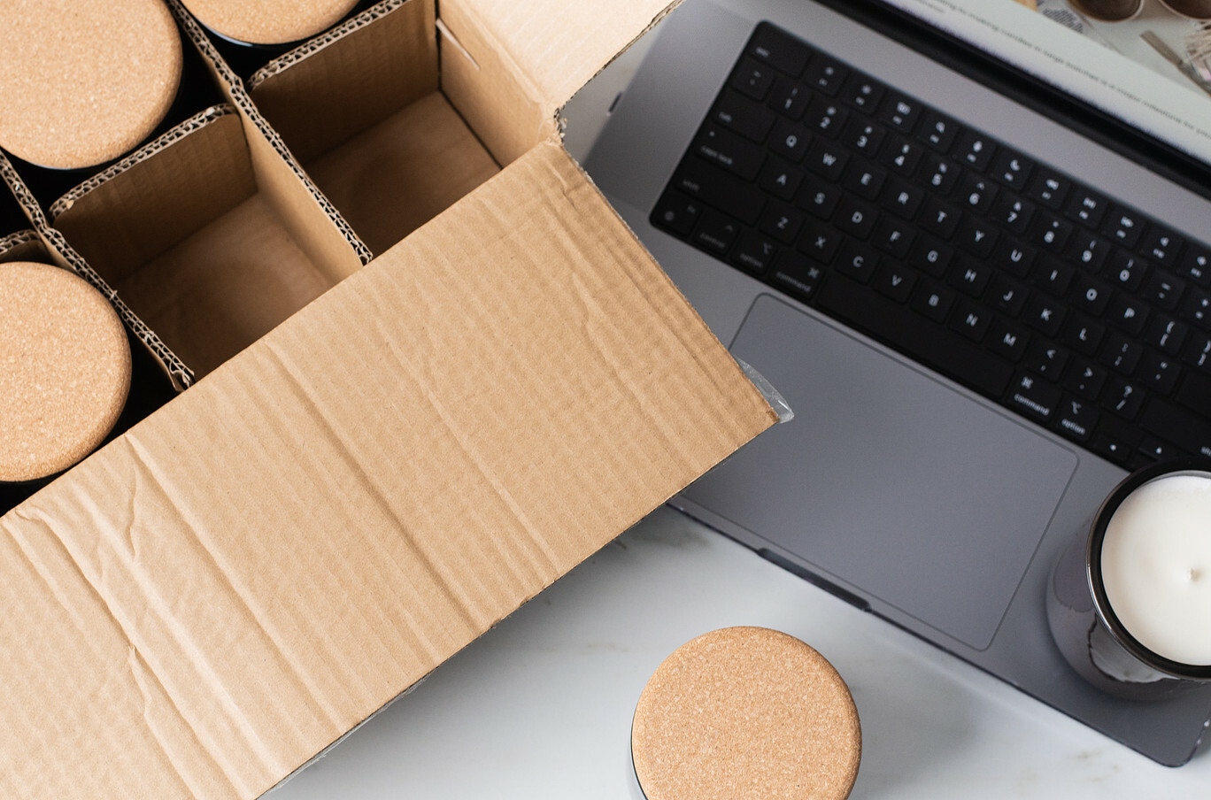 An opened box of wholesale candles next to a silver laptop that is open. 