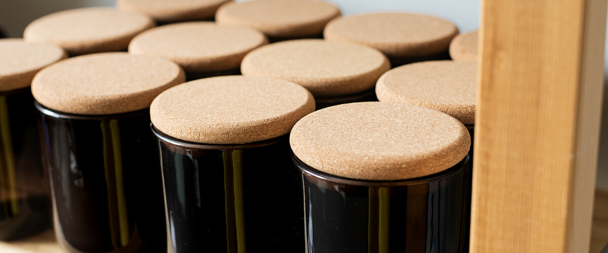 Candles in black jars with cork lids lined up on a shelf