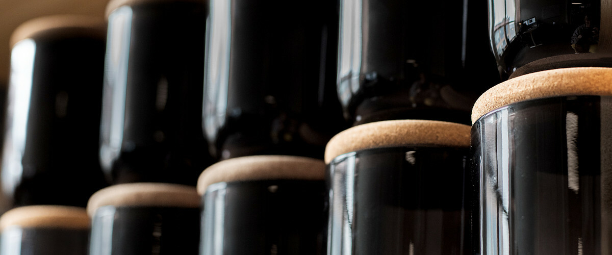 Two rows of candles in black glass jars with cork lids