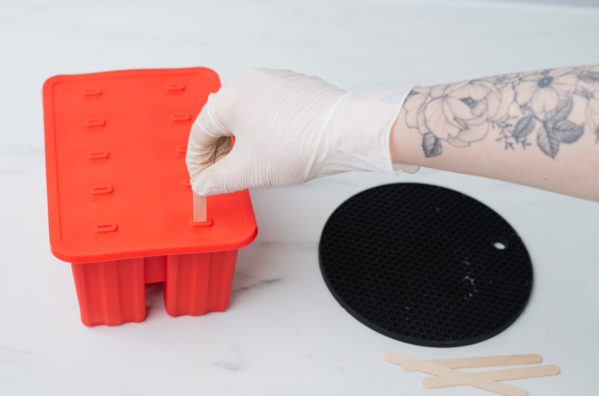 Placing popsicle sticks into melted soap base and silicone mold.