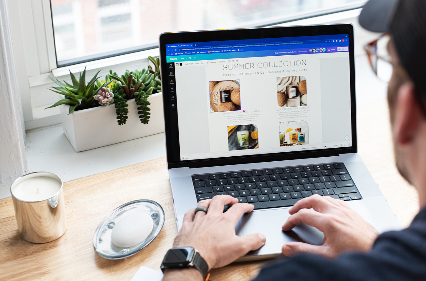 An over-the-shoulder view of a light-skinned man with glasses creating a wholesale catalog in Canva on a laptop.