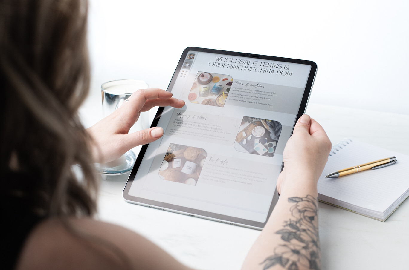 An over-the-shoulder view of a light-skinned woman reviewing a wholesale line sheet on an iPad