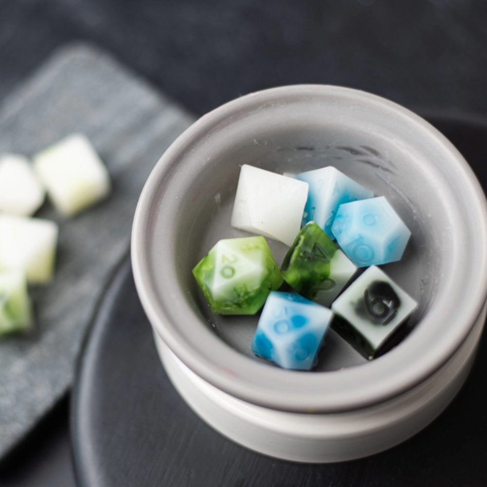 A gray wax melter with wax melts in blue, green, black, and white shaped like 20-sided die.