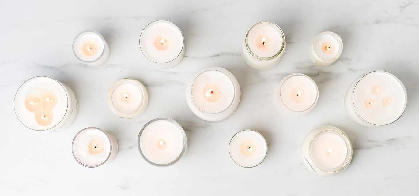 An overhead view of a horizontal grouping of lit container candles sits on a marble surface