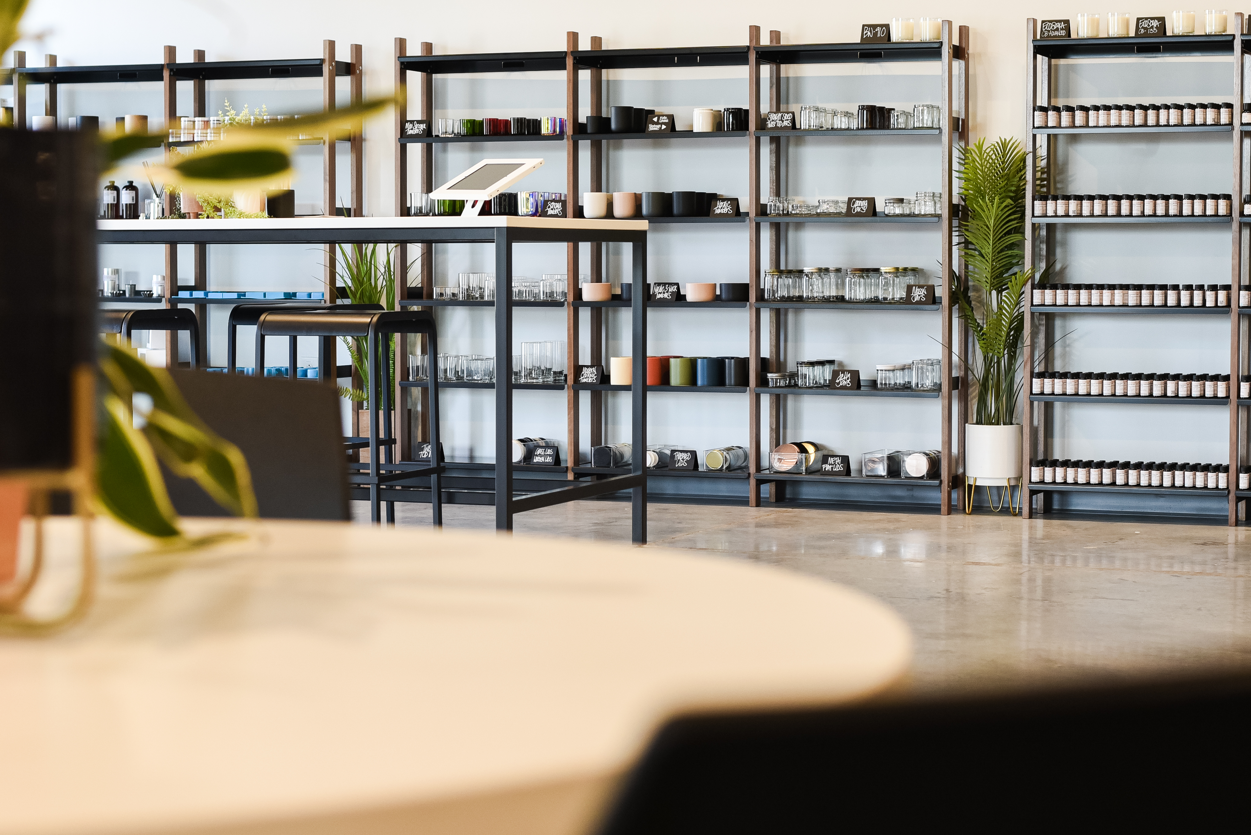 A white table is in the foreground, shelves lined with candle containers and other products are in the background.  