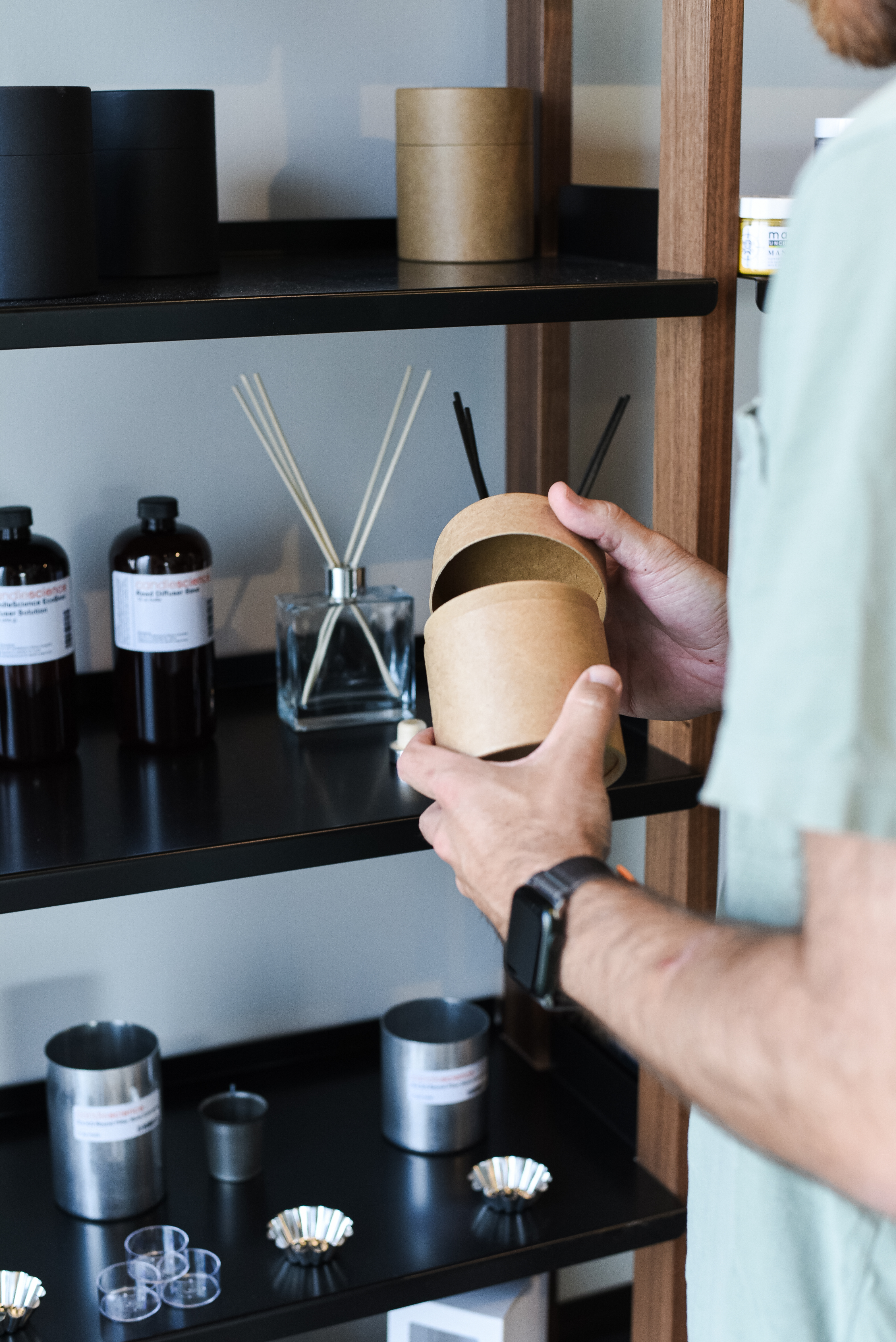 A person at a candle supply store holds a cardboard packaging tube while standing near an assortment of other products. 