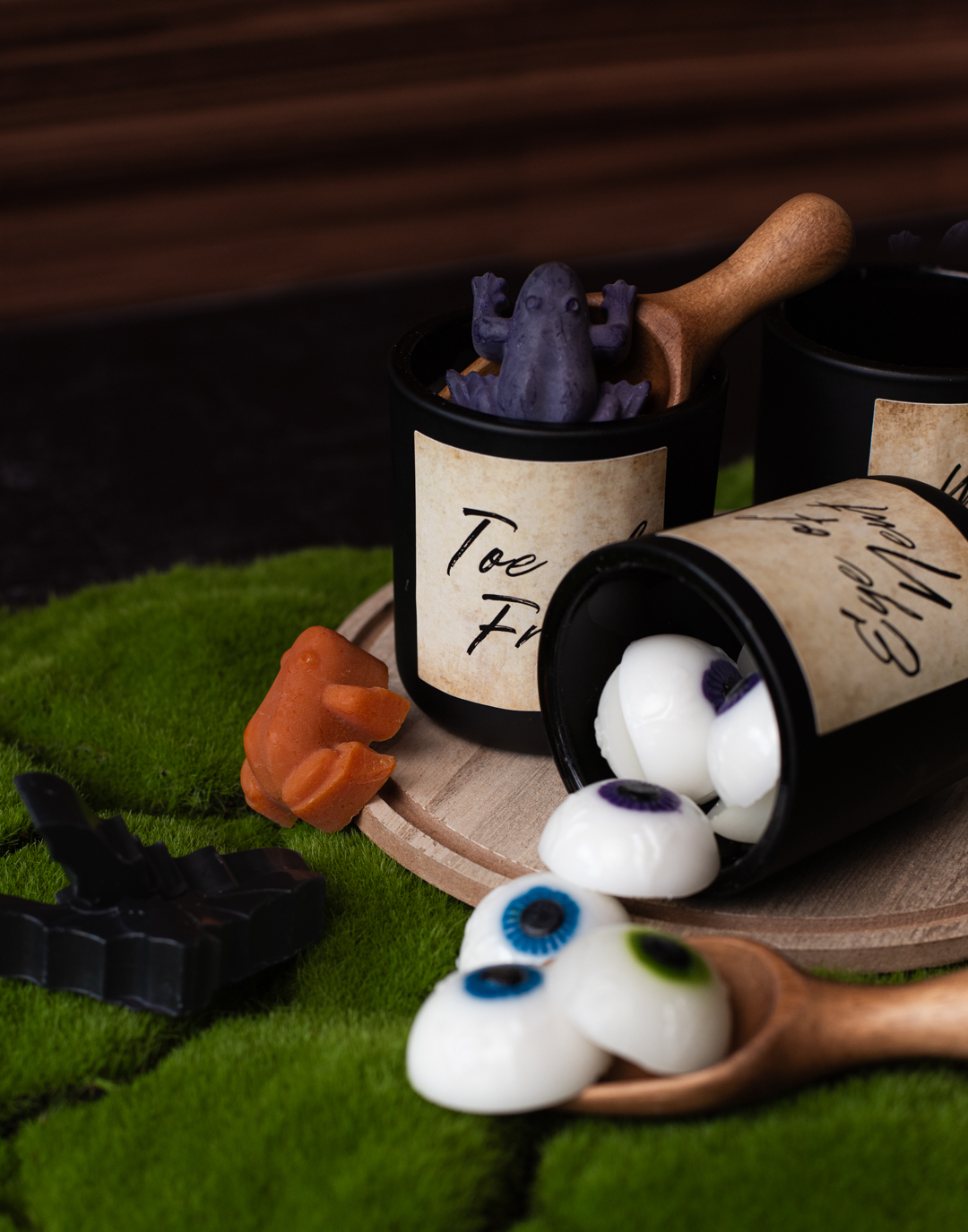 Wax melts inspired by witch's brew ingredients, eye of newt, toe of frog, and wool of bat. Pictured are eyeball wax melts with blue, green, and purple irises, frog wax melts dyed orange and purple, and bat wax melts dyed black.