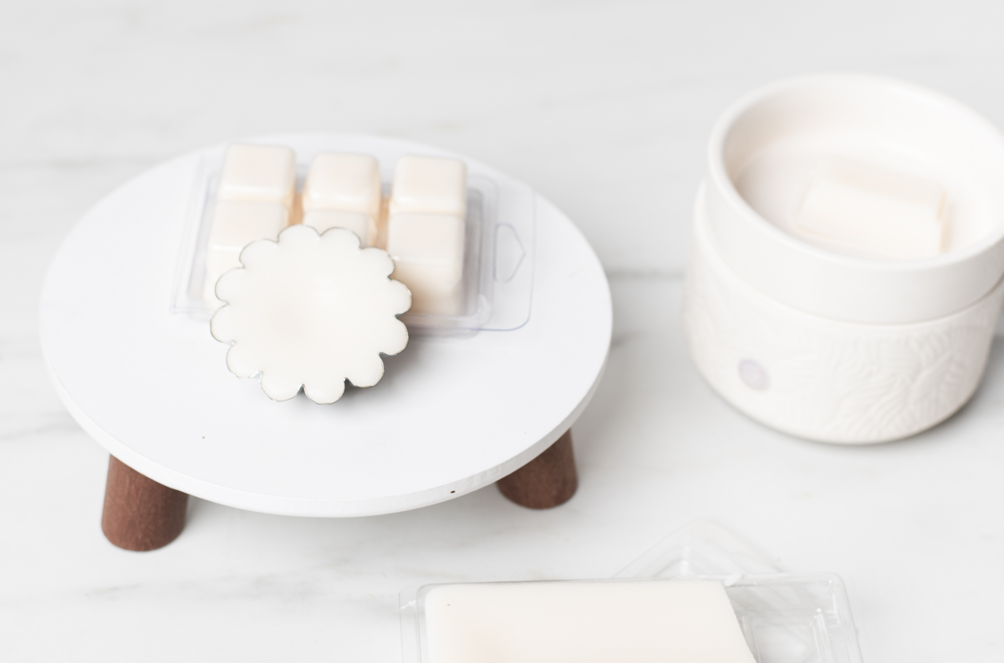 White wax melts are displayed on a white marble surface. One wax melt is shaped like a flower and one is a wax melt clamshell.