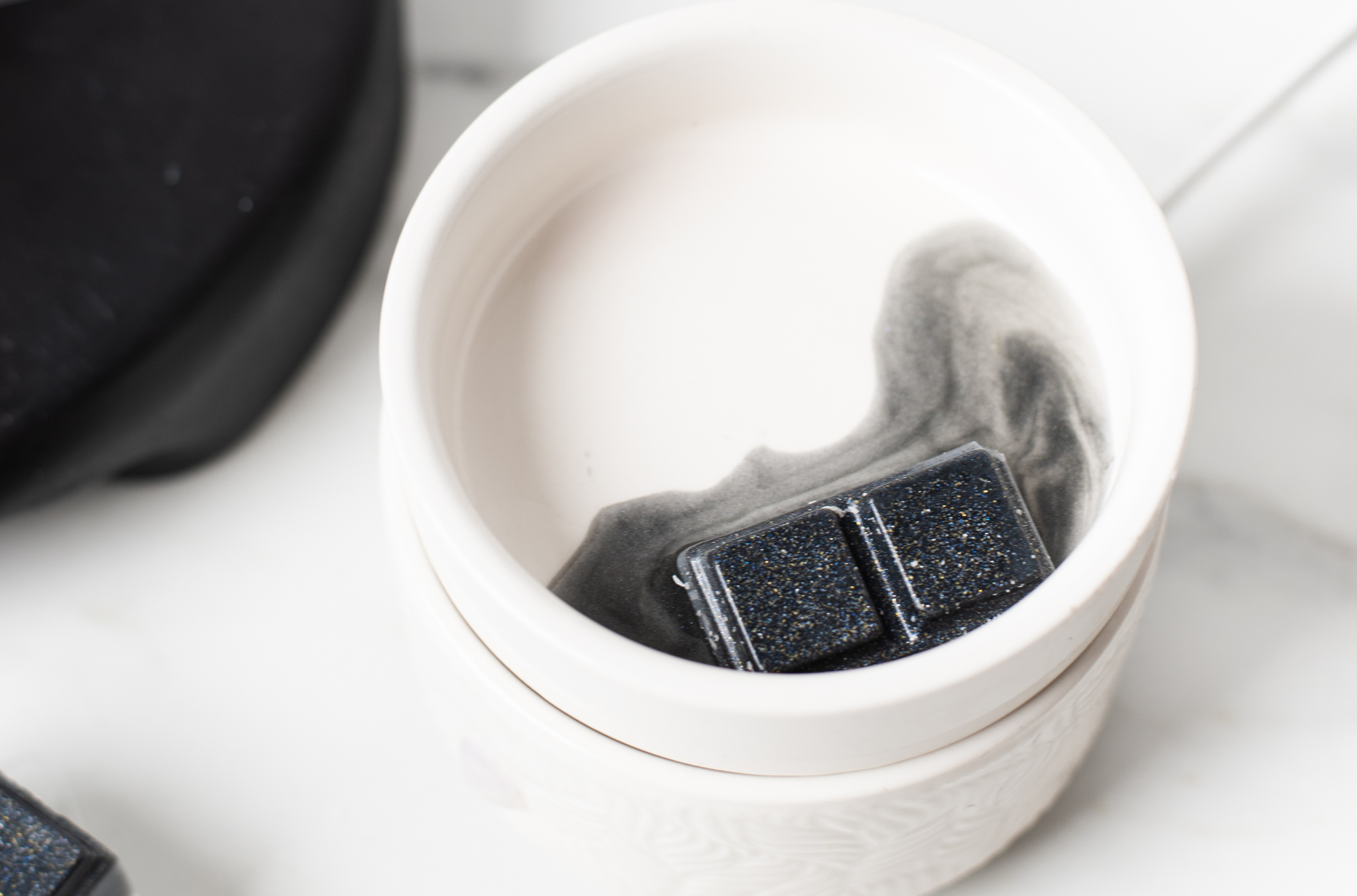 A top-down photo of a white wax melter with black wax melting in it. 