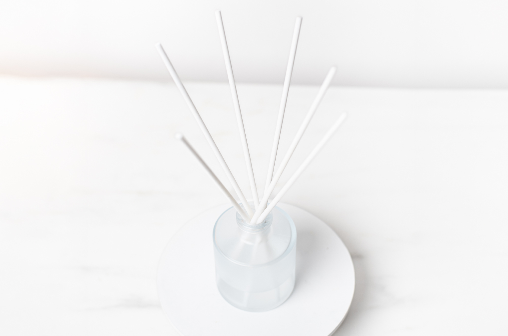 A reed diffuser with white diffuser reeds in a frosted, round bottle.