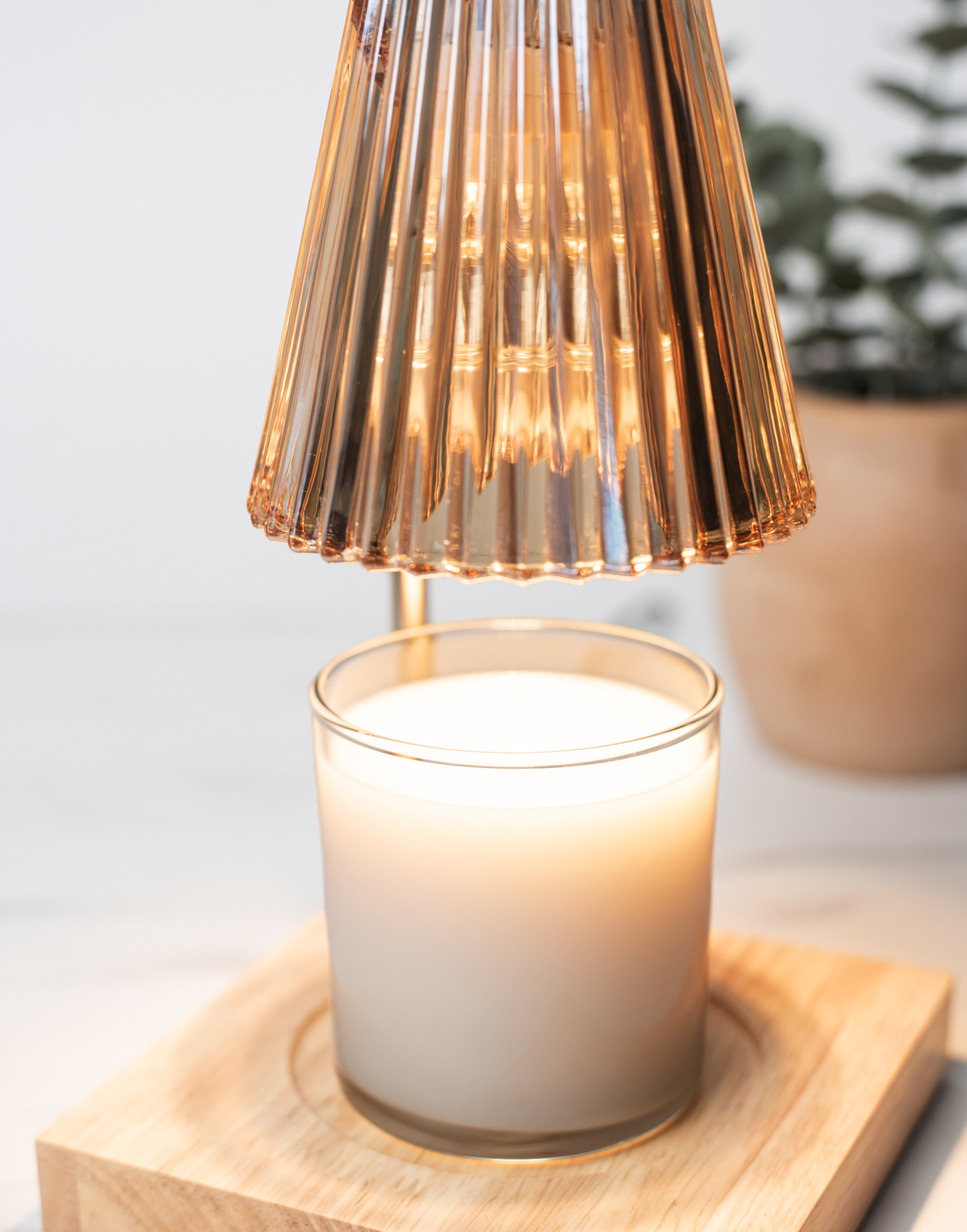 A white wickless candle melting under a candle warming lamp. 