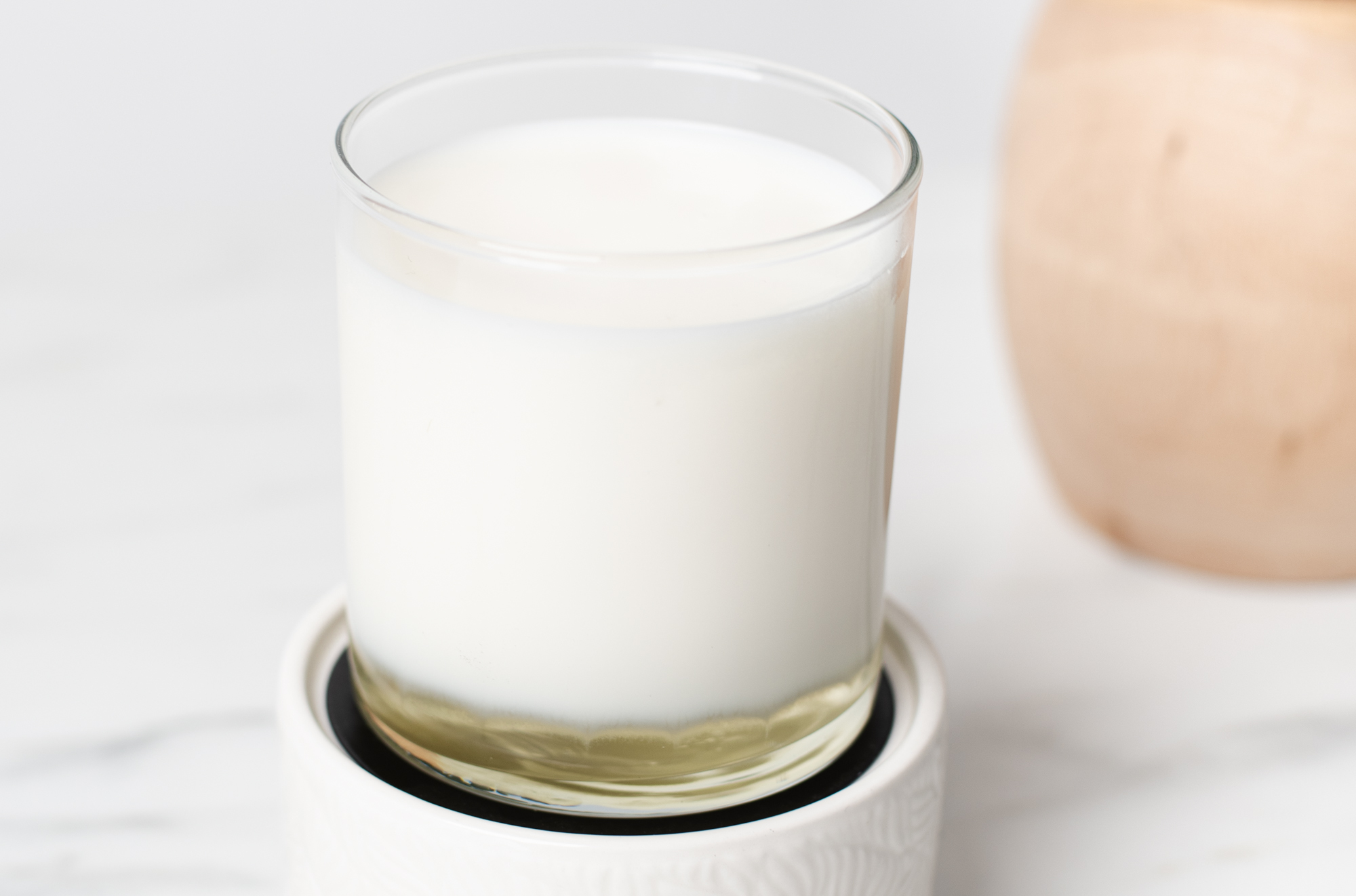 A wickless candle melting on a candle warmer. The candle container is glass, revealing white wax melting from the bottom. 