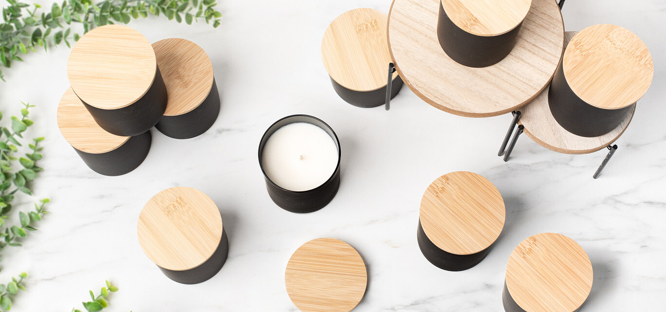 An overhead view of black candle containers with natural bamboo lids on a marble background