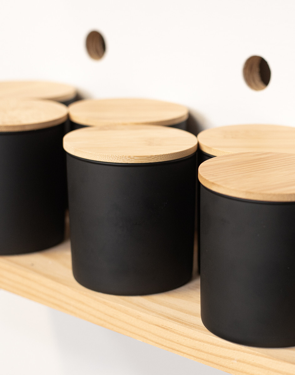 Black candle containers with natural bamboo lids are lined up on a shelf