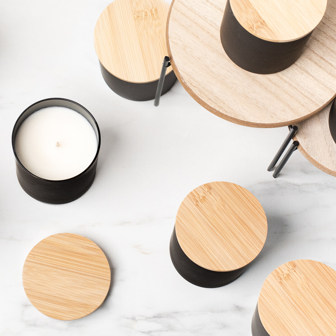 An overhead view of black candle containers with natural bamboo lids on a marble background.