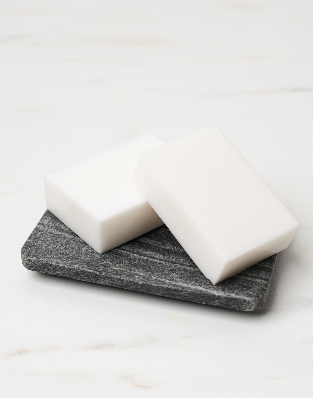 Two white rectangular bars of soap are laid on a tabletop to cure.