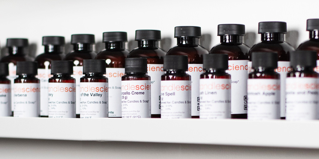 An array of fragrance oils in amber bottles with CandleScience labels on a shelf. 