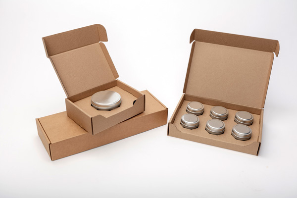 Two Flush Packaging cardboard shipping boxes are open to display candle tins from CandleScience