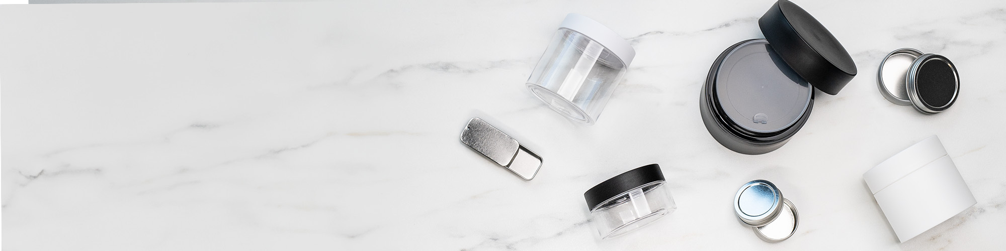 A variety of cosmetic packaging - sliding tins, 4 oz and 8 oz clear and double walled jars in black and white. 