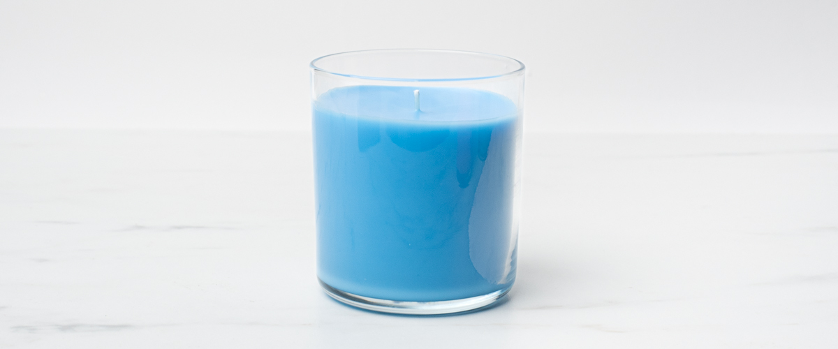 A clear straight sided tumbler jar using CandleScience Coconut Apricot Wax dyed blue showing a wet spot on the side.