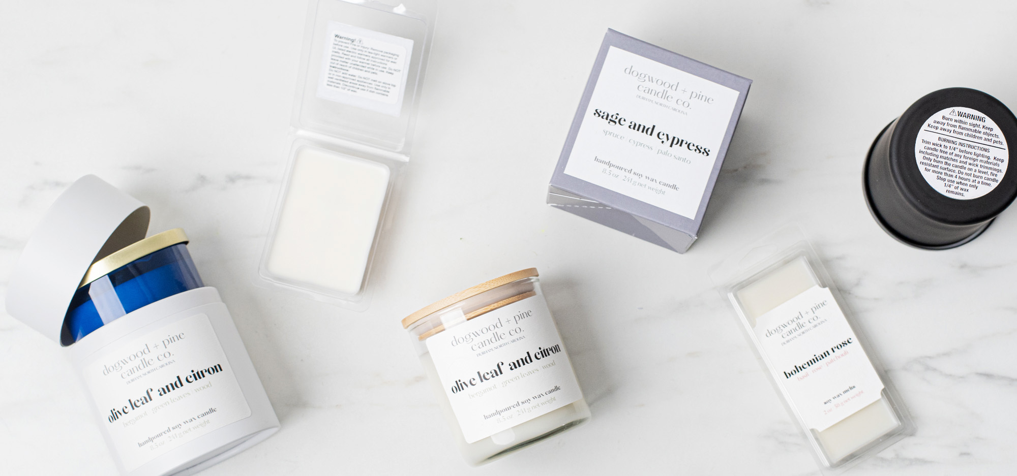 An assortment of candles and wax melts featuring examples of product labels and warning labels arranged in a flatlay on a white marble surface.