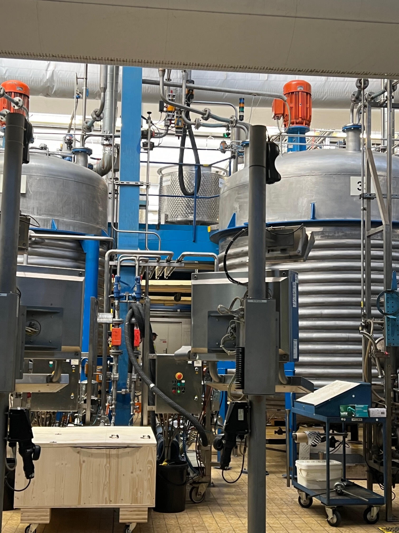 Large silver metal tanks in a fragrance oil manufacturing facility connected together by a complex series of pipes and other machinery.