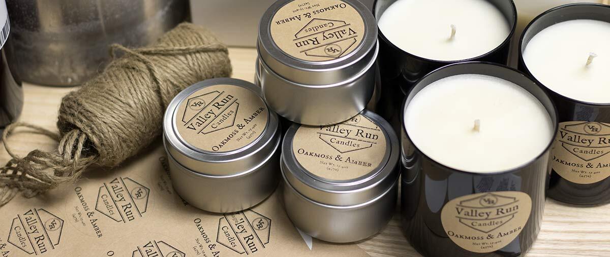 Candles in silver tins with kraft paper labels stacked on a wood surface