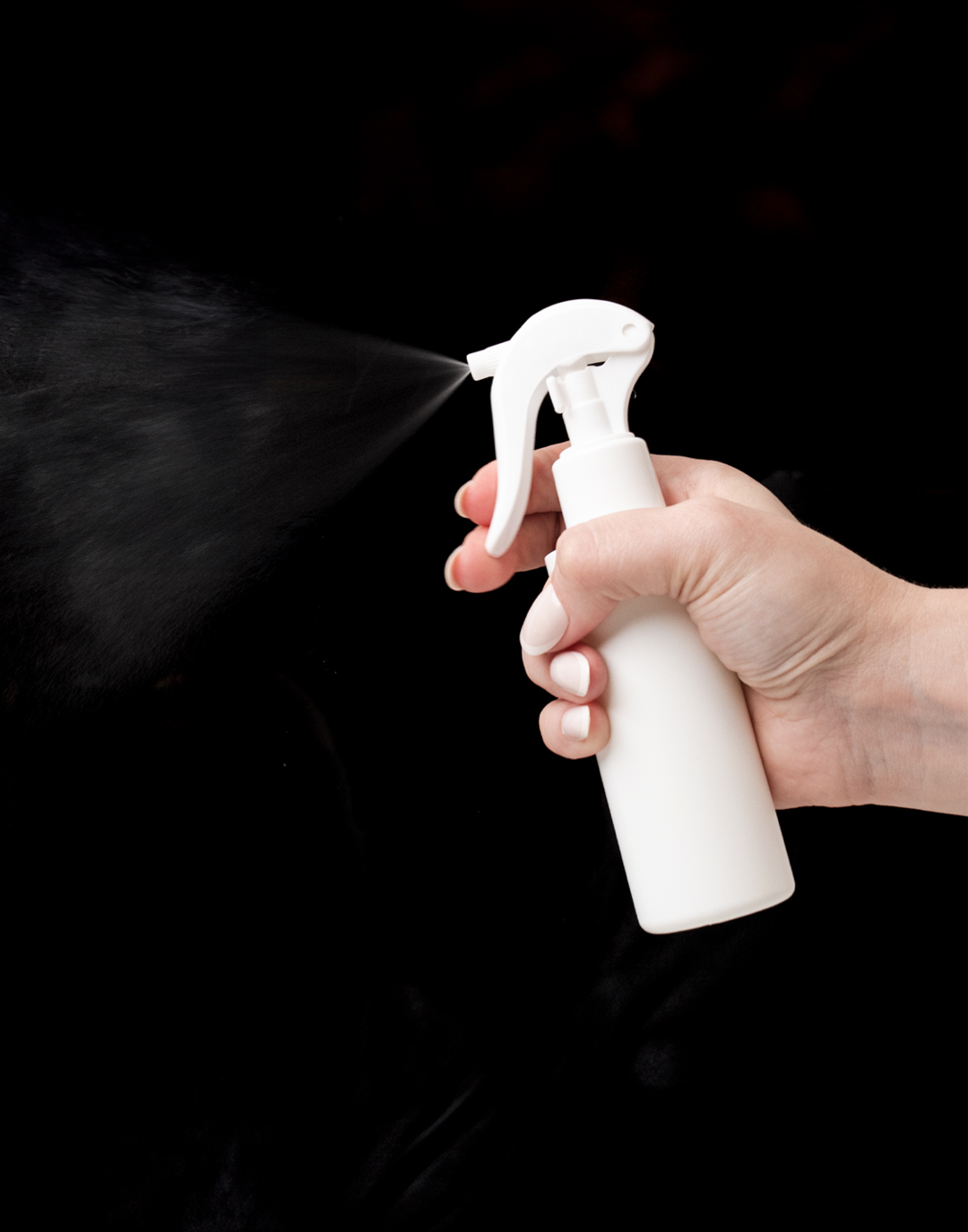 Spraying bottle in front of a dark background.