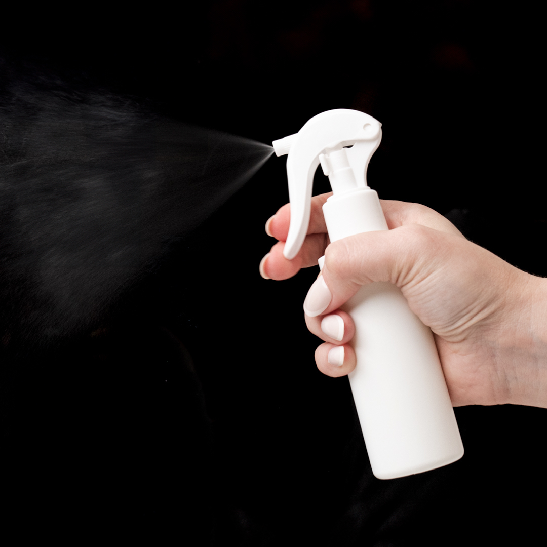 A room and linen spray bottle with a fine mist on a black background.