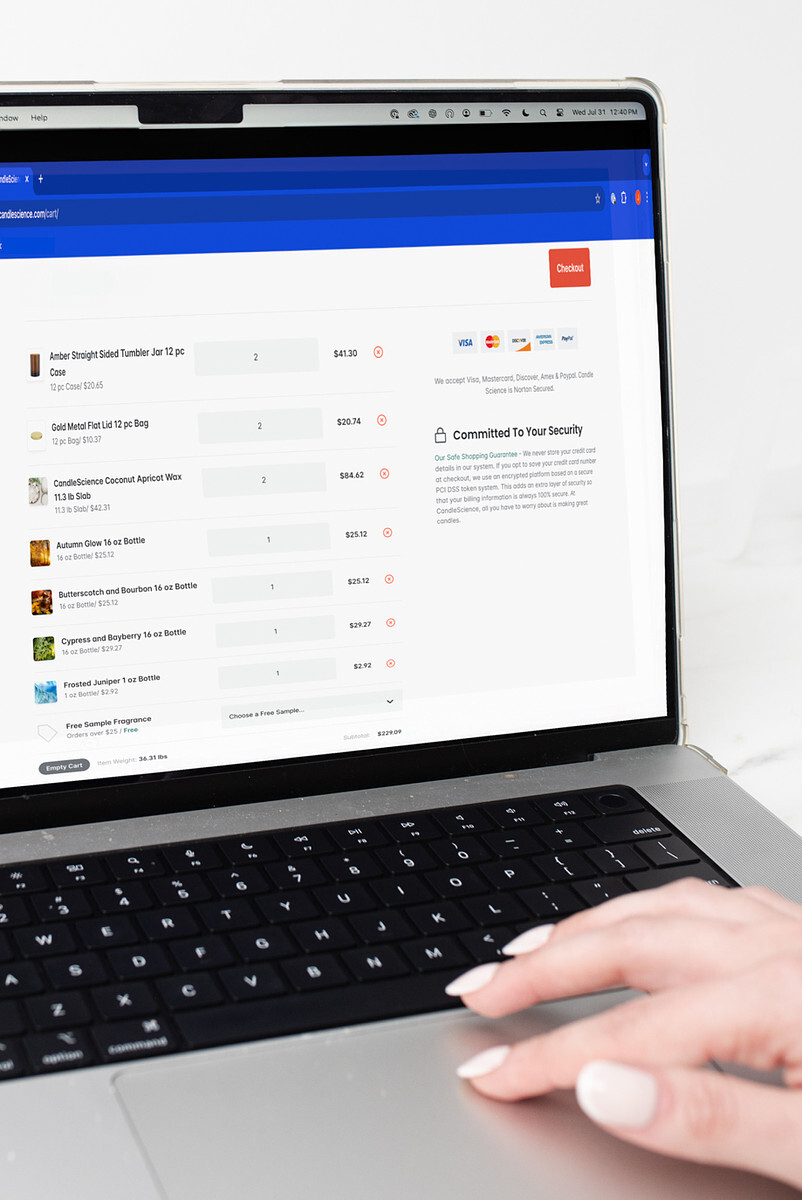 A light-skinned hand gestures on a laptop that displays the shopping cart for an online order at CandleScience.